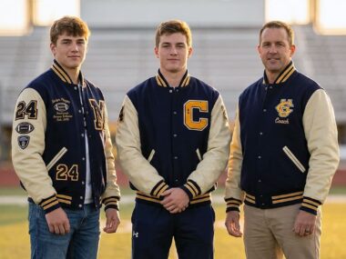 Seniors, captain, and coach wearing custom letterman jackets on a U.S. field