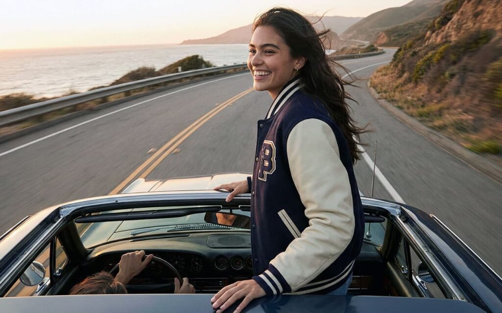 girl standing in open roof car wearing varsity jacket outfits.
