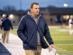high school football coach wearing navy coach jacket on sideline